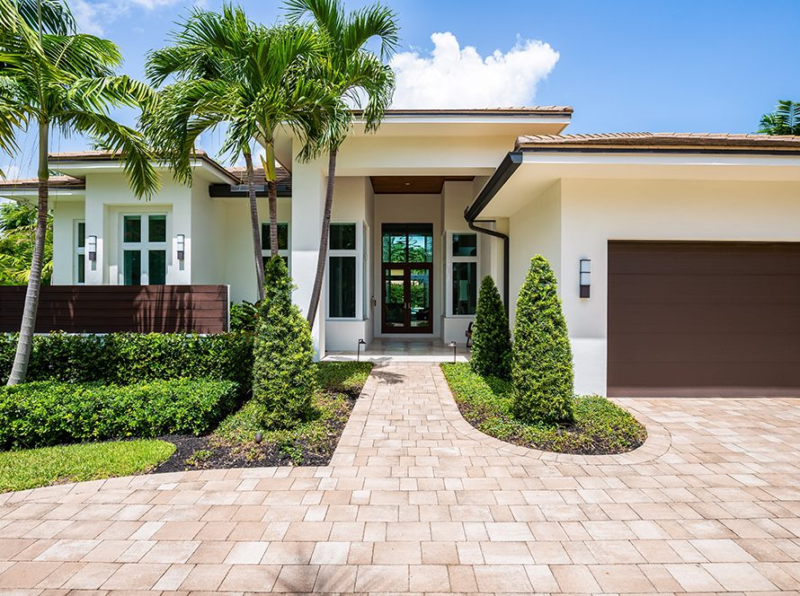 Facade of a beautiful house, with a front garden made up of palms, short grass and tropical plants, in Coral Ridge in Miami, driveway, sidewalk and street